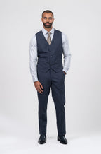 Man wearing a navy suit vest and pants with a white shirt and tie on a white background